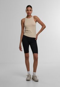 Beige ärmelloses Top und schwarze, knielange Leggings. Das Top hat einen runden Ausschnitt und ein kleines Logo, während die Leggings eine glatte Textur und feine Nähte aufweisen.