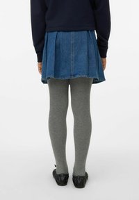 Falda de mezclilla con pliegues, lavado oscuro, con dobladillo sin terminar, combinada con leggings grises y bailarinas negras con textura. Vista trasera, estilo casual.