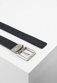 Cintura in pelle nera con una finitura testurizzata, dotata di una fibbia rettangolare in metallo silver e multiple fori per la regolazione.