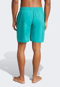 Tirkizne kupaćice s elastičnom trakom u struku i bočnim džepovima, s glatkom, laganom teksturom i dužinom iznad koljena.