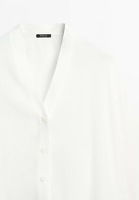 White button-up shirt with a V-neck collar, showing the top three buttons and a black label inside the collar.