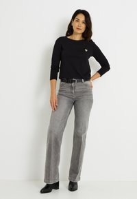 Top negro de manga larga con un pequeño logo de corazón, combinado con jeans grises de pierna recta y botines negros. Conjunto simple y casual.