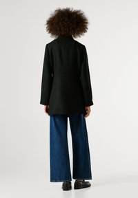 Melna, piegriezta mēteli ar augstu apkakli un garām piedurknēm, kopā ar platām deminss biksēm. Gluda auduma struktūras piegriezums.