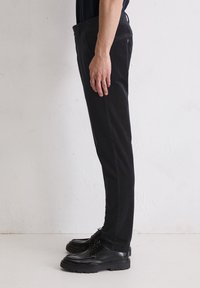 Zwarte, slim-fit broek met een gladde textuur, voorzien van een tailleband met een knoop, zijzakken en een rechte pijp. Gemaakt in combinatie met zwarte schoenen.