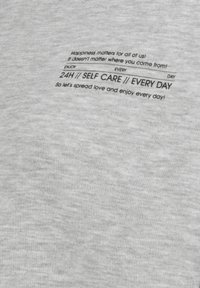 Grau geknitterter Stoff mit subtiler Textur, bedruckt mit schwarzem Text: "Happiness matters... 24H // SELBSTFÜRSORGE // JEDEN TAG." Schlichtes, modernes Design.