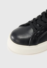 Μαύρο δερμάτινο αθλητικό παπούτσι με στρογγυλεμένη μύτη, μαύρα κορδόνια και λευκή ελαστική σόλα. Διαθέτει λεία υφή και λεπτομέρειες ραφής.