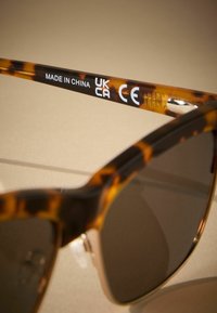 Naočale od kornjače s tamnim staklima, s glatkim sjajem. Bočna ruka prikazuje oznake "MADE IN CHINA", "UKCA" i "CE".
