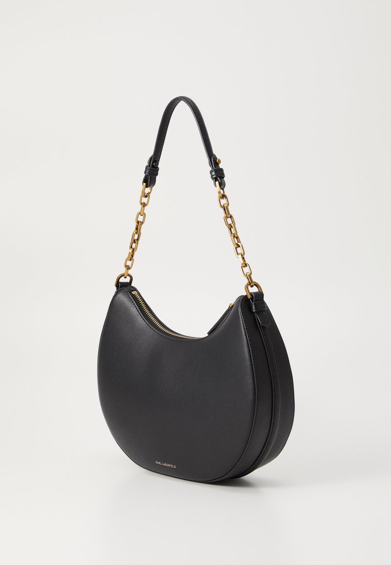 Schwarze Lederhandtasche in Halbmondform, mit einem Kettenhenkel in Goldfarbe und einem Reißverschluss oben. Glatte Textur, dezente Markenkennzeichnung sichtbar.
