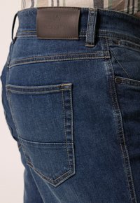 Tmavě modré džíny z denimu s koženou nášivkou označenou "BOSTON PARK", kontrastním prošíváním a zaoblenou zadní kapsou.