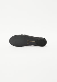 Black flat shoe with a textured upper and a smooth rubber sole. Features gold branding on the sole and a rounded toe design.