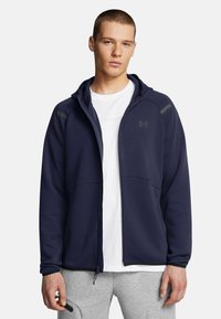Navy zip-up hoodie made of soft fabric featuring a fitted design, contrasting gray accents, and two front pockets.