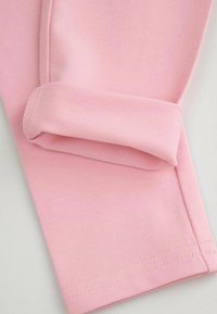 Różowa tkanina, zbliżenie na zwinięty mankiet o gładkiej fakturze i widocznych detalach szwów. Prosty design bez wzorów czy akcentów.