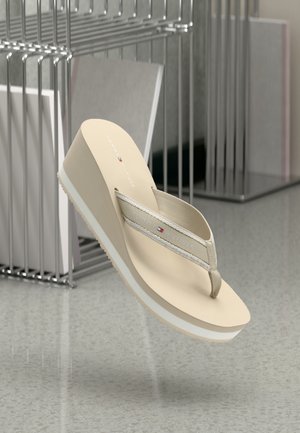 Beige sleehak slippers met een gestructureerde band, voorzien van een wit accent op de zool en "TOMMY HILFIGER" branding op de band.