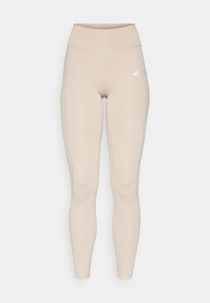 Leggings de talle alto en color beige, elaborados con tela elástica, que cuentan con costuras planas, un bolsillo lateral y un pequeño logo blanco. Textura suave.