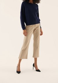 Marinblå ribbad stickad tröja med sänkta axlar, i kombination med beige cropped byxor med fransade fållar och svarta stilettklackar.