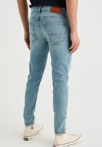 Světle modré džíny z denimu s úzkým střihem, s koženou nášivkou na zadním pásu a dvěma zadními kapsami. Dokončeno bílými vysokými teniskami.