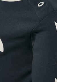 Svart bomullströja med vitt designelement; har ribbad struktur, rund halsringning och sidostygn med en cirkulär detalj.