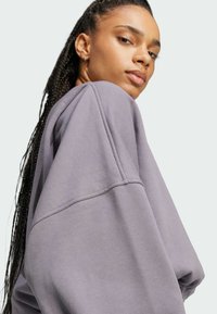 Felpa oversized viola con una texture morbida e spalle cadenti. Presenta dettagli cuciti e una vestibilità rilassata.