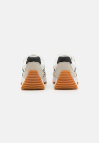 Baskets blanches avec un talon beige texturé, une semelle crantée orange et des détails noirs. Présente une tige lisse et des accents embossés.