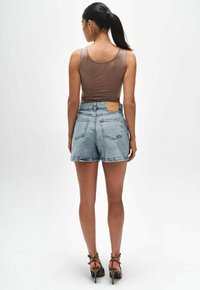 Bruin aansluitend hemdtop, hoogwendige lichtblauwe denimshorts met rafelige zomen, en een bruine leren label op de tailleband. Geklede sandalen maken de look compleet.