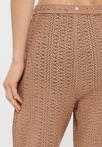 Ανοιχτό καφέ πλεκτά παντελόνια με υφασμάτινο λουλουδάτο σχέδιο, που διαθέτουν ψηλή μέση και κλείσιμο με ένα κουμπί.