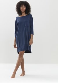 Navyblauwe jurk tot de knie met driekwartmouwen, een losse pasvorm en een enkele borstzak. Zachte, gladde textuur met zijsplitsen.