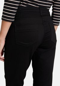 Svarta tajta jeans med en slät yta, med hög midja och två bakfickor med synliga sömdetaljer.