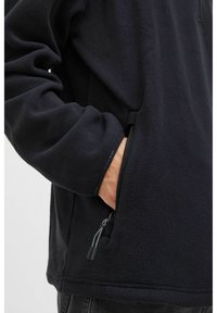 Pullover en polaire noir au style décontracté, avec une poche latérale zippée et un cordon de serrage ajustable à l'ourlet pour un maintien sûr.