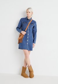 Τζιν φόρεμα με μακριά μανίκια, μπροστινά κουμπιά, δύο τσέπες στο στήθος. Συνδυασμένο με καφέ σουέτ μποτάκια μέχρι τον αστράγαλο και τσάντα crossbody με φούντες που ταιριάζει.