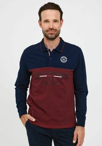 Polo majica s dugim rukavima u tamnoplavim i burgundskim dijelovima, s ovratnikom, logotipom i tekstualnim detaljima u kontrastnoj boji.