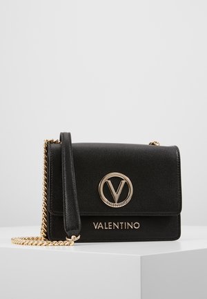 Zwarte leren schoudertas met gouden kettinkje als band, voorzien van een circulair logo en gouden letters. Getextureerd materiaal met een gestructureerd ontwerp.