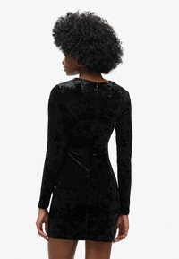 Vestido de terciopelo negro con mangas largas, diseño ajustado y cierre de cremallera en la espalda. Textura suave y Silueta elegante.