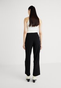 Calças pretas de cintura alta com um corte descontraído, combinadas com uma blusa branca sem mangas. Apresentam uma textura suave e um design de perna larga.
