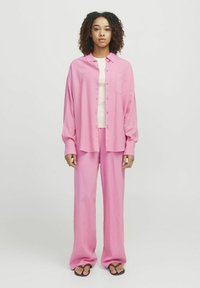 Roza srajca z dolgimi rokavi in širokimi hlačami. Svetla majica pod njo. Gladek material z udobnim krojem. Preprost dizajn.