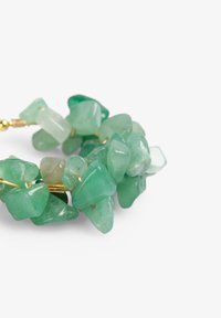 Pulsera de piedra verde compuesta por piedras semitranslúcidas pulidas e irregulares de diversos tonos de verde, ensartadas en un alambre dorado.