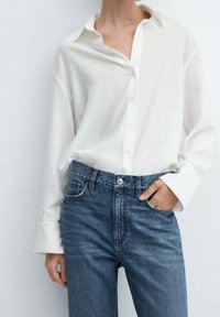Camicia bianca con bottoni in un tessuto leggero, dal taglio ampio e con maniche larghe, abbinata a jeans in denim blu a vita alta.