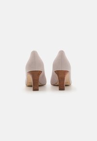 Light gray suede high heels with a rounded toe and a wooden block heel. The sole is beige, featuring minimal branding.