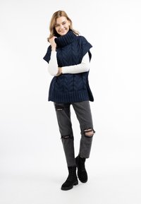 Marineblå strikket turtleneck poncho med et kabelmønster, parret med grå ripped jeans og sorte snørestøvler. Glat tekstur, afslappet pasform.