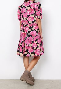 Květinové šaty Flo s krátkými nafouknutými rukávy, černým pozadím, velkými růžovými a béžovými květinami, vrstevnatou sukní a kombinované se světle hnědými kotníkovými botami.