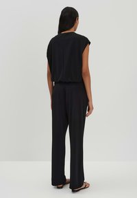 Zwarte, loszittende top met kapmouwen en een gathered zoom, gecombineerd met wijde broekspijpen. Soepele textuur en minimalistisch ontwerp.