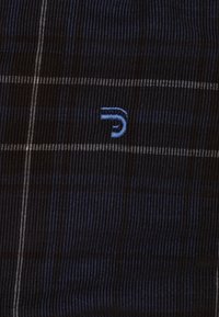 Zwart en marineblauw geruite stof met blauwe borduursels featuring een gestileerde "D" logo. Textuurweefsel met dunne witte accentlijnen.