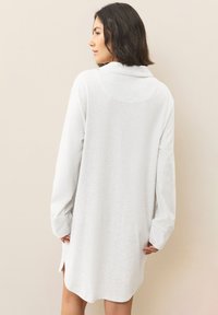 White long-sleeve shirt dress with a collar, side slits, and a relaxed fit. Made from lightweight, soft fabric with a smooth texture.