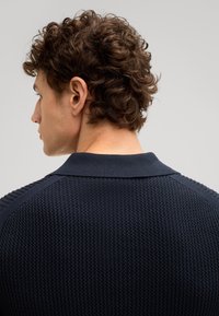 Marine gebreide trui met een gestructureerde stof, geribbelde kraag en schouderaccenten. Close-up van het ontwerp achterop en de halslijn.