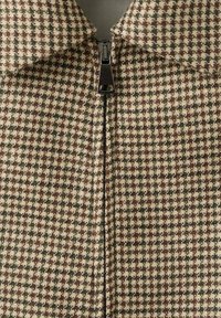 Kurtka z tkaniny w wzór pepitki z czarnym zamkiem błyskawicznym z przodu i kołnierzem złożonym.