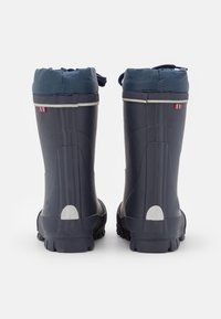 Un paio di stivali impermeabili blu scuro con bordi imbottiti e lacci, visti da dietro su uno sfondo bianco.