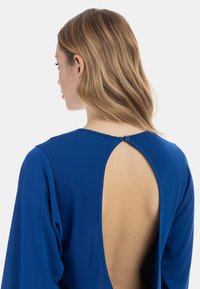 Kleid in Königsblau mit langen Ärmeln und offener Rückenpartie, runder Ausschnitt und kleiner Knopfverschluss hinten. Glatte Textur.