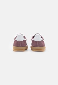 Lila mockaskinnssneakers med vita detaljer och gummisula. Har en låg design och vadderad krage, lämpliga för vardagsbruk.