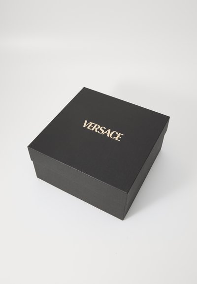 Boîte carrée noire avec une texture lisse, arborant une marque dorée "VERSACE" bien visible sur le couvercle. Construction solide et rigide.