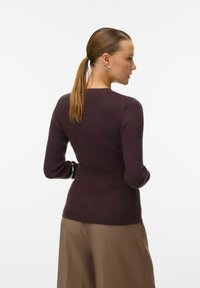 Burgundy ribbad stickad tröja med långa ärmar och rund halsringning, tillsammans med vida beige byxor. Slät textur, figurnära design.