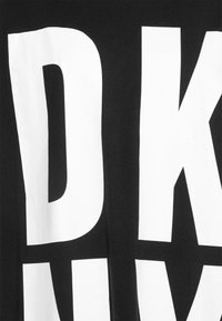 T-shirt noir avec de grandes lettres blanches en bloc. Le texte affiche en évidence "DKNY." Le matériau semble doux et légèrement texturé.